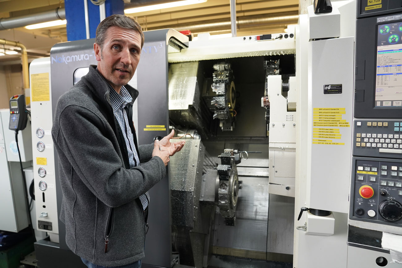 Der Geschäftsführer Hans Langesee erklärt seine leistungsstärkste CNC-Maschine: Sie ist an das Kühlsystem angeschlossen und kann deshalb Temperaturschwankungen besser vorbeugen. So sind Präzisionsarbeiten auf bis zu einen sechs- bis neuntausendstel Millimeter genau möglich.